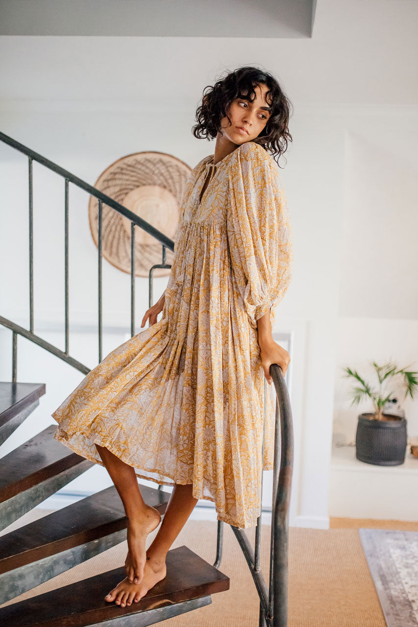 Daughters of India Kyra Midi Dress in Cumin — leaning on spiral staircase, flowing skirt, billowed sleeves