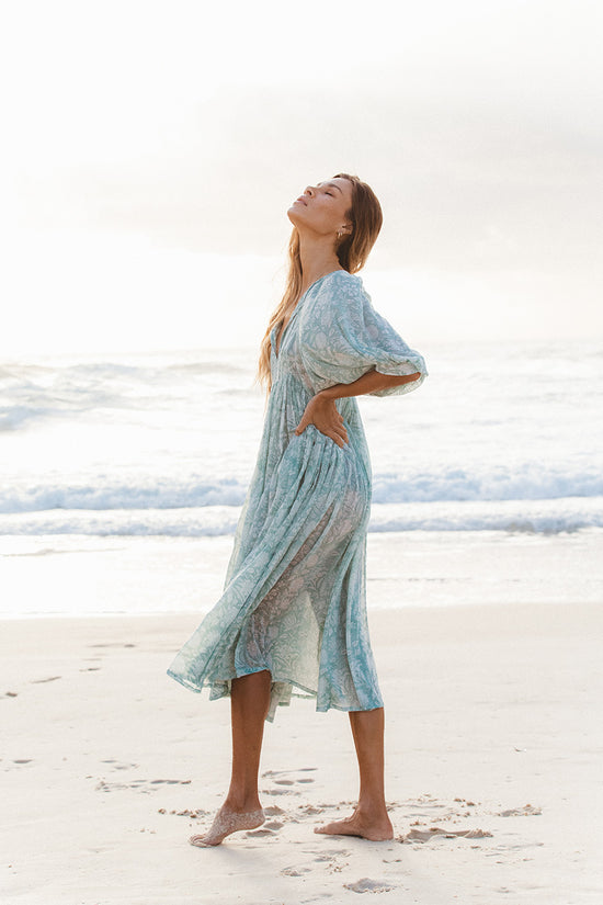 Woman wearing Daughters of India Kyra Midi Dress in Jade on a beach, dress flowing in the breeze with head tilted back