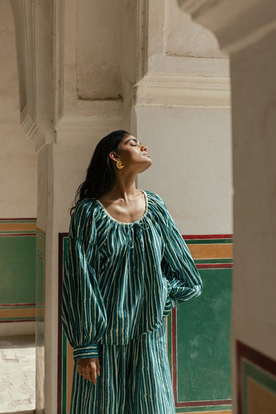 Ria Blouse Cyan Candy — lifestyle doorway portrait, model standing in colourful architectural setting wearing cyan and dark stripe hand block print cotton blouse, artisan Jaipur India | Daughters of India