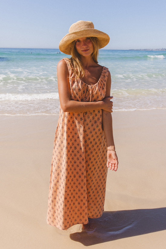 Sundress Midi Peach — full length beach portrait, model in straw hat, sleeveless silhouette with tie-gather neckline and A-line skirt, hand block print peach floral cotton, artisan Jaipur India | Daughters of India