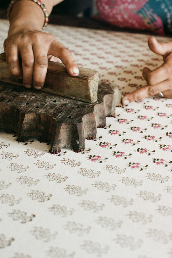 Sundress Mini Peony — close-up of hand-carved wooden block and peony floral print being stamped on cotton fabric, traditional block printing craft Jaipur India | Daughters of India